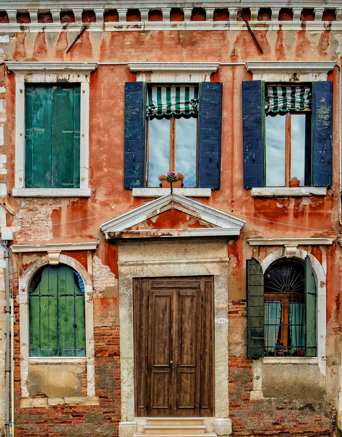 Verwitterte Hausfassade mit abblätternder Farbe und bunten Holzläden.