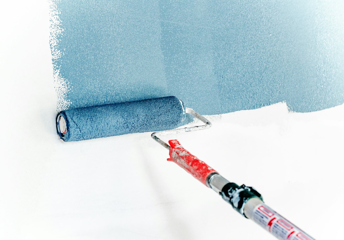 Farbroller trägt hellblaue Farbe auf eine weiße Wand auf.